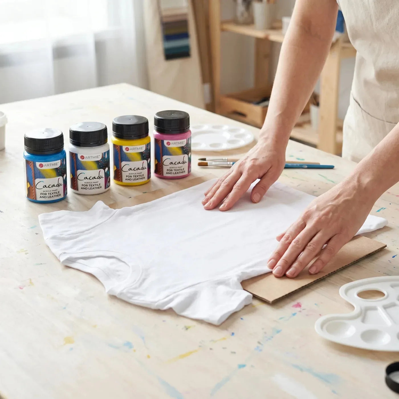 Netezirea unui tricou alb cu carton în interior, alături de vopsele Cacadu pentru textile