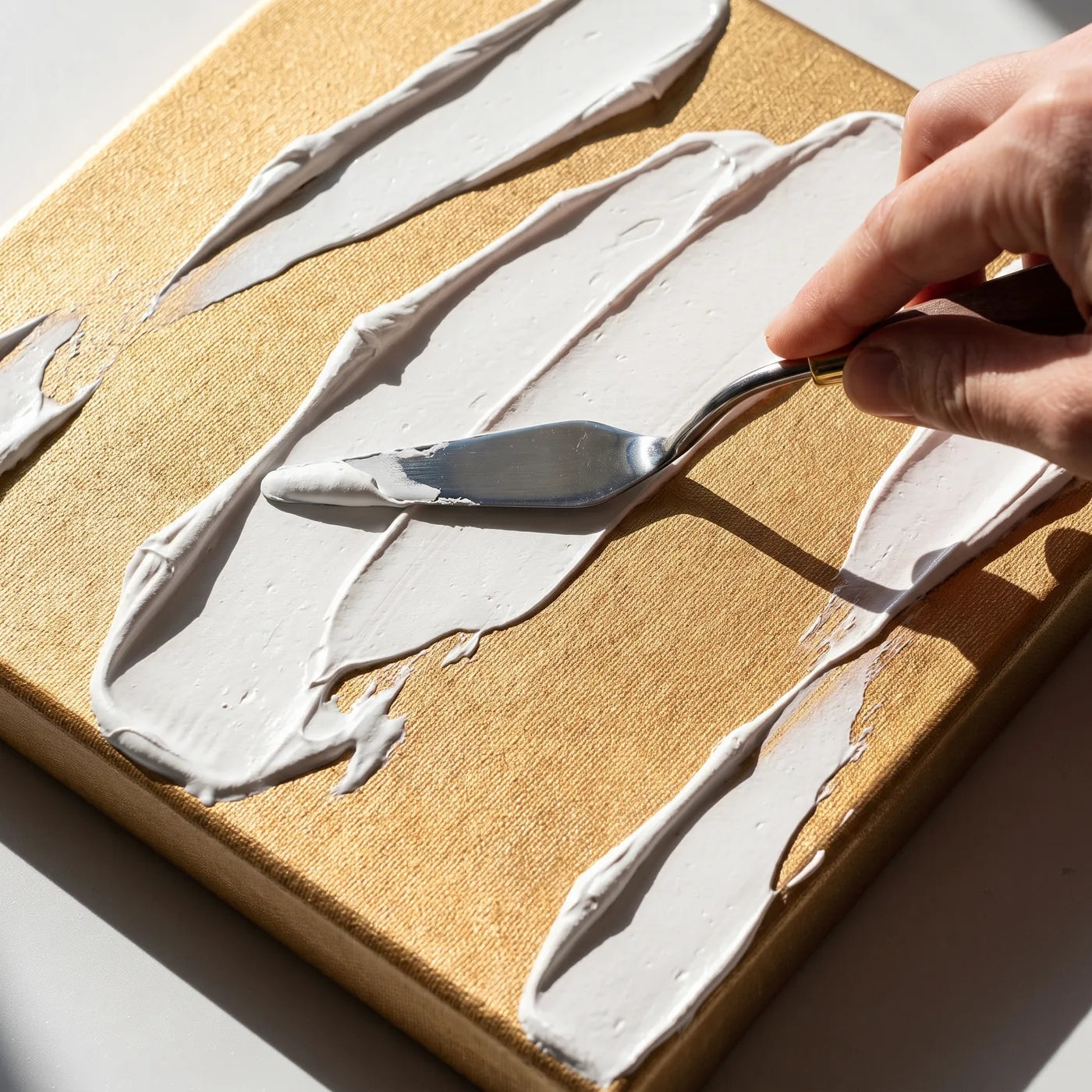 Pastă structurată albă aplicată cu spatula pe pânza aurie MIDAS